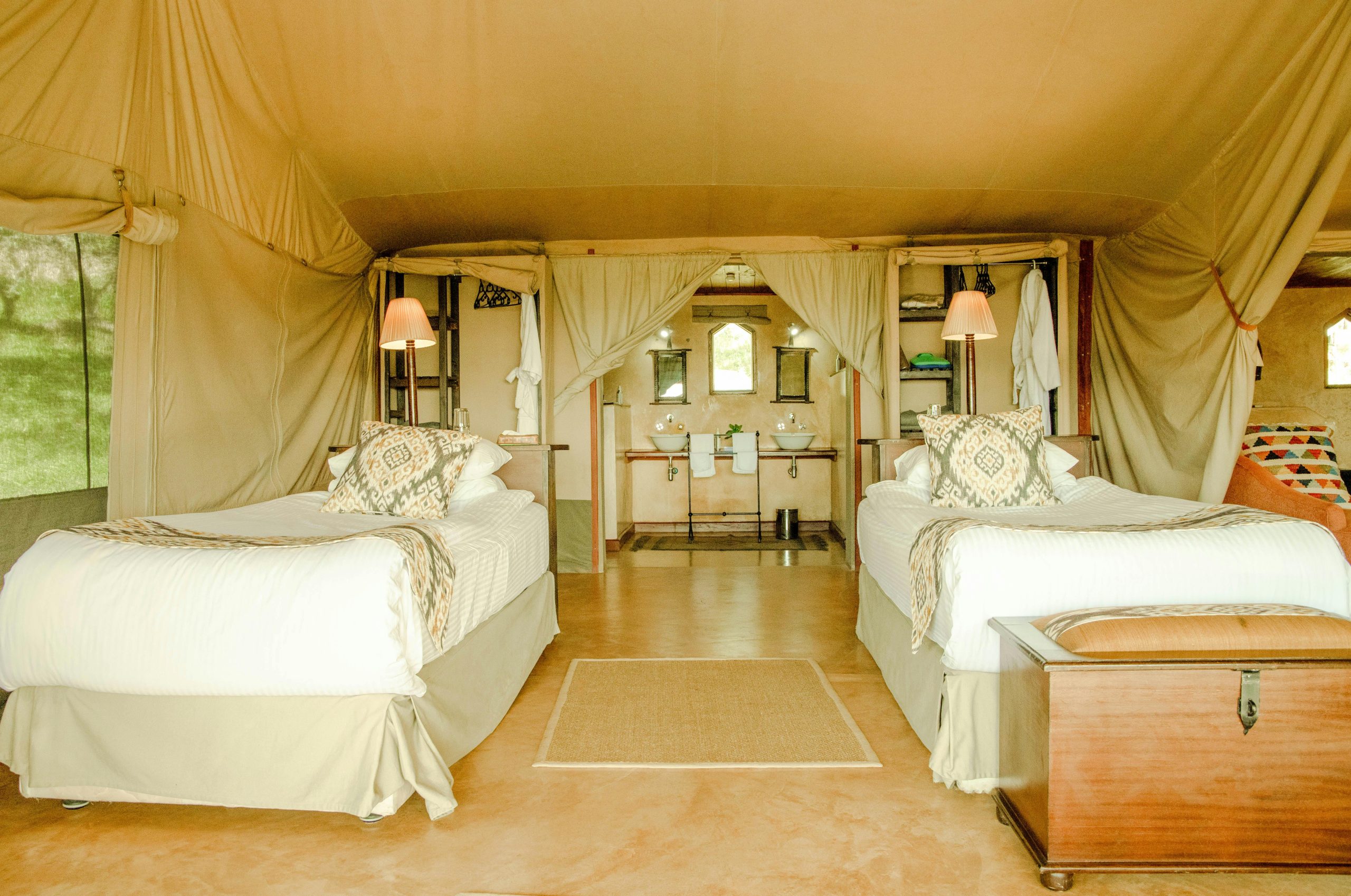 Elegant safari tent interior with twin beds and rustic decor, embodying luxury camping vibes.